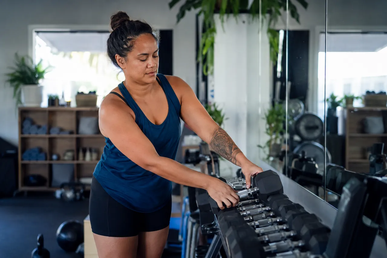 A gym owner racking dumbbells on the floor of her training studio