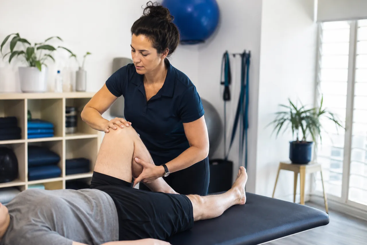 A physiotherapist assessing a client's knee on a treatment table in a clinic
