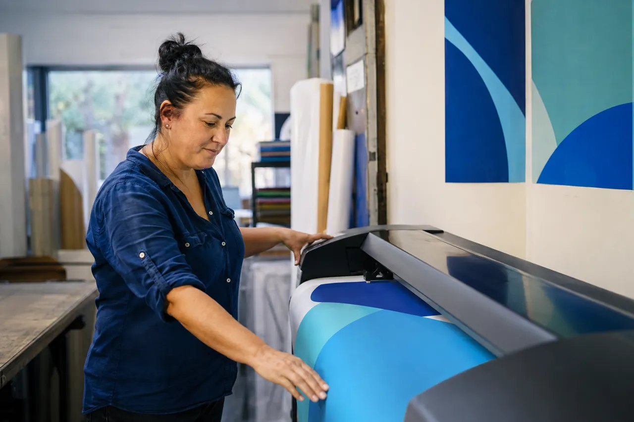 A woman feeding printed stock through a large-format printer in a signage workshop