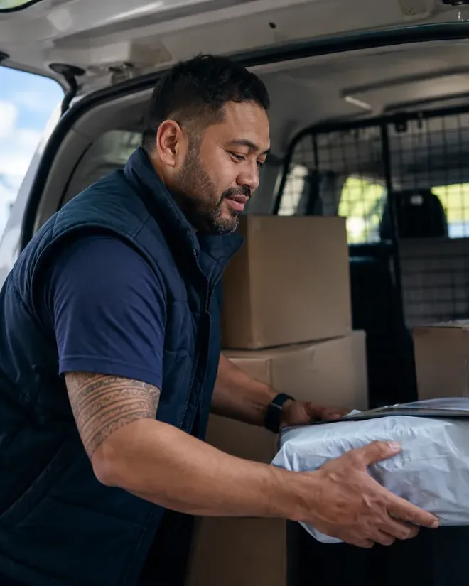 A courier lifting a parcel into the back of a van at the kerb