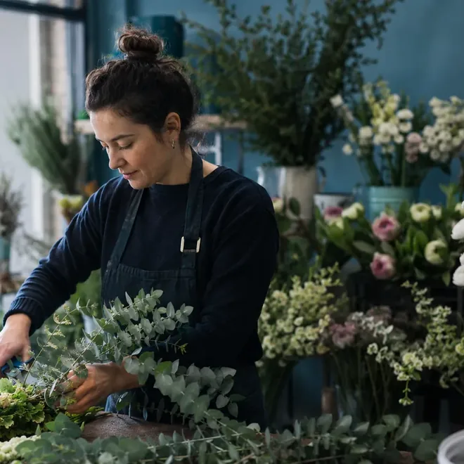 A florist trimming eucalyptus stems at a workbench in her shop