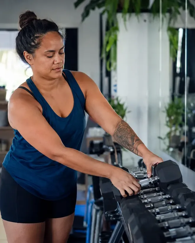 A gym owner racking dumbbells on the floor of her training studio