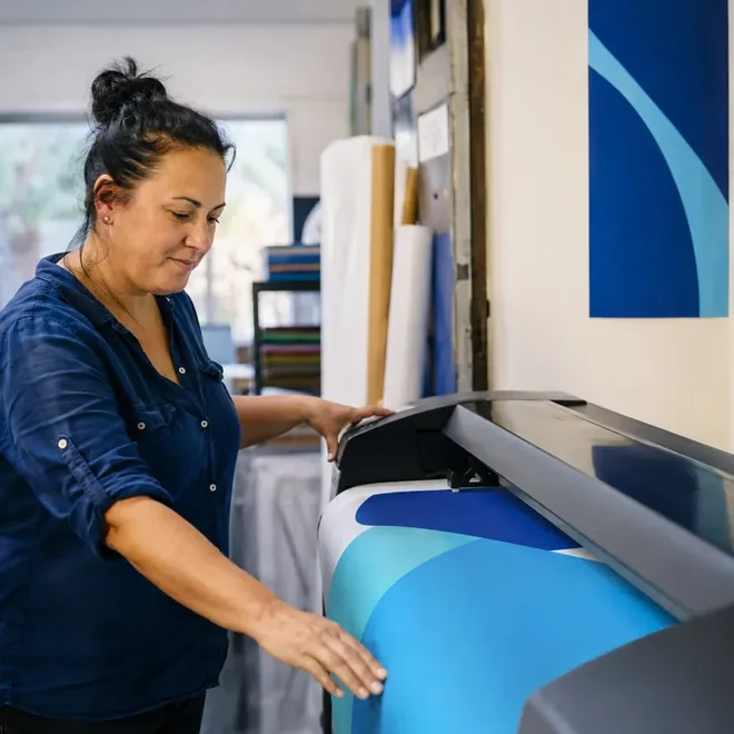 A woman feeding printed stock through a large-format printer in a signage workshop