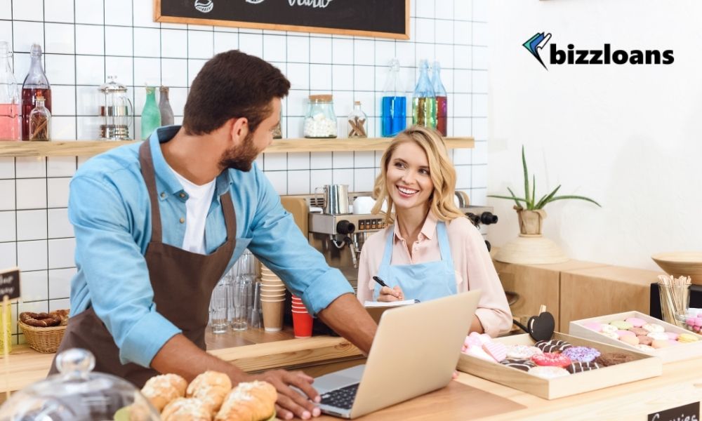 two cafe owners using a laptop in the counter while smiling at each other