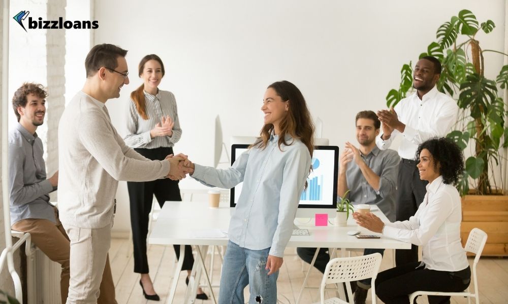 Manager congratulating a female staff in front of other employees in the office