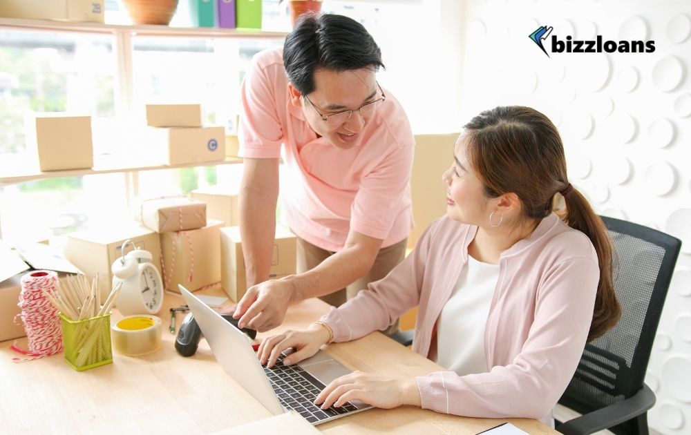 two business owners smiling at each other while checking on how to improve financial position in the laptop