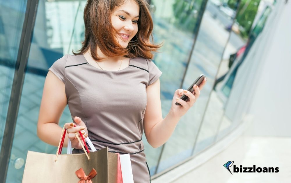 Happy fashion woman with shopping bags using mobile phone, shopping center