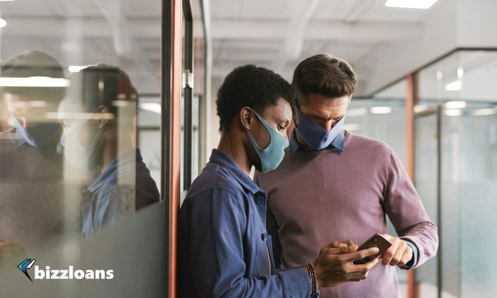 two small business owners looking at a smartphone wearing masks in the office