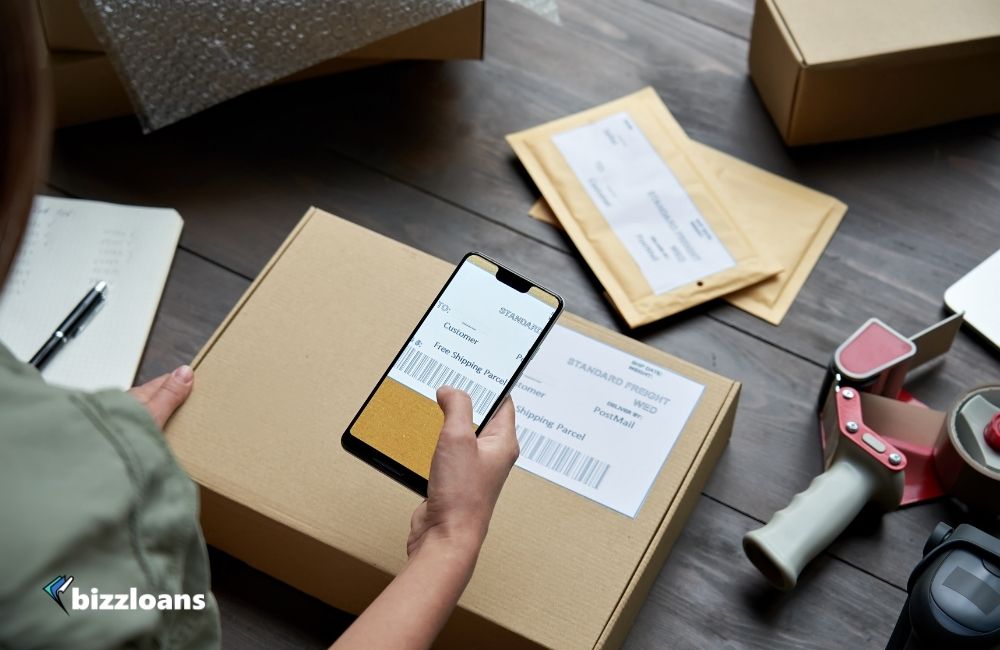 Small business owner holding phone scanning retail package postal parcel barcode on ecommerce shipping box label on smartphone using mobile app, close up. 