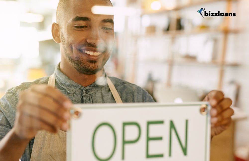 smiling business owner holding an "Open" sign in his shop