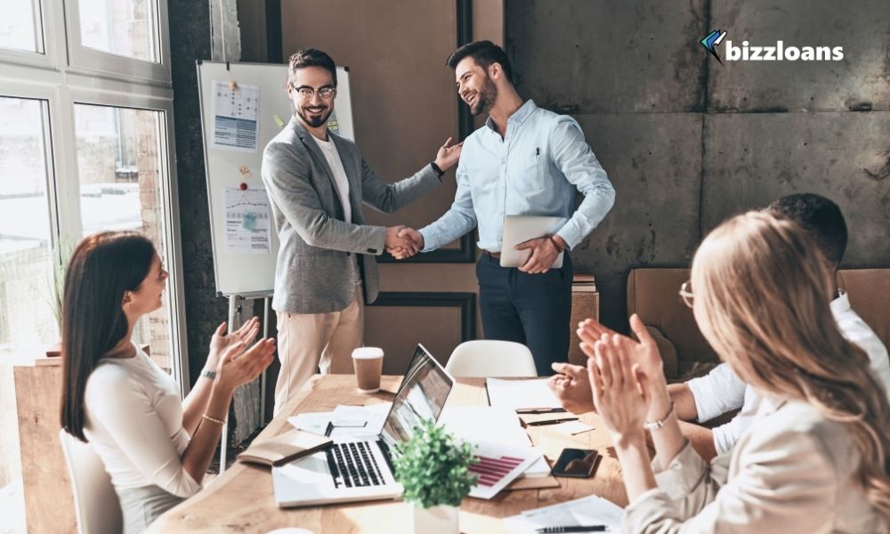 male leader congratulating a male employee in front of his staff in the office; leadership skills concept