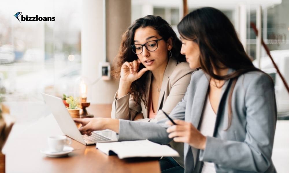 two female business owners discussing in coffee shop in front of laptop