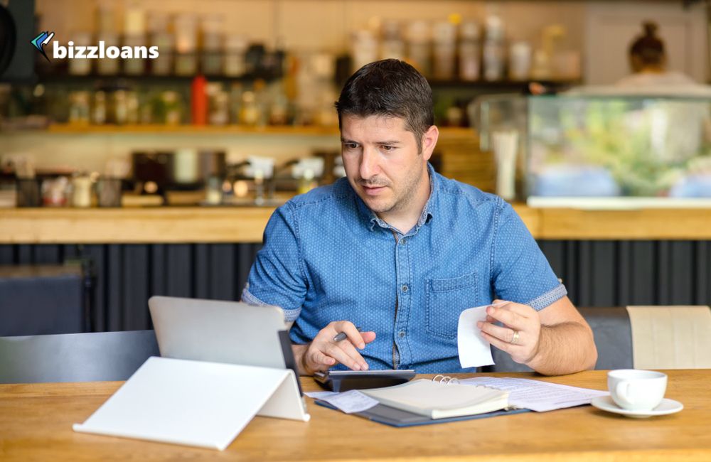 male business owner in his restaurant using calculator and tablet to refinance business loan